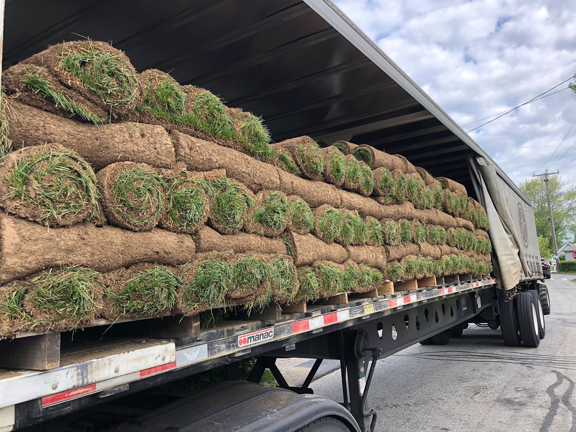 A semi truck filled with rolls of grass is parked on the side of the road.