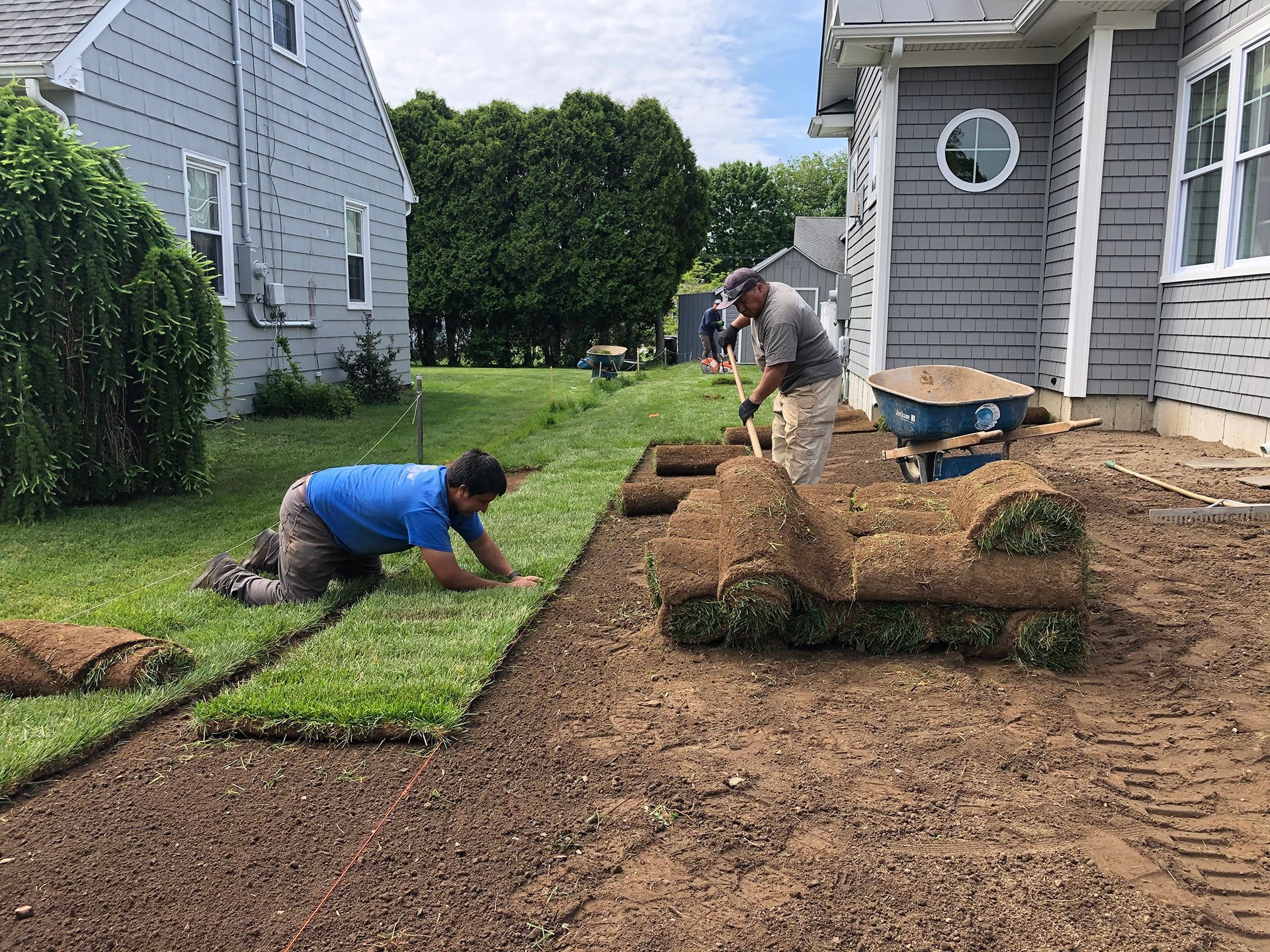 Two men are working on a lawn in front of a house.