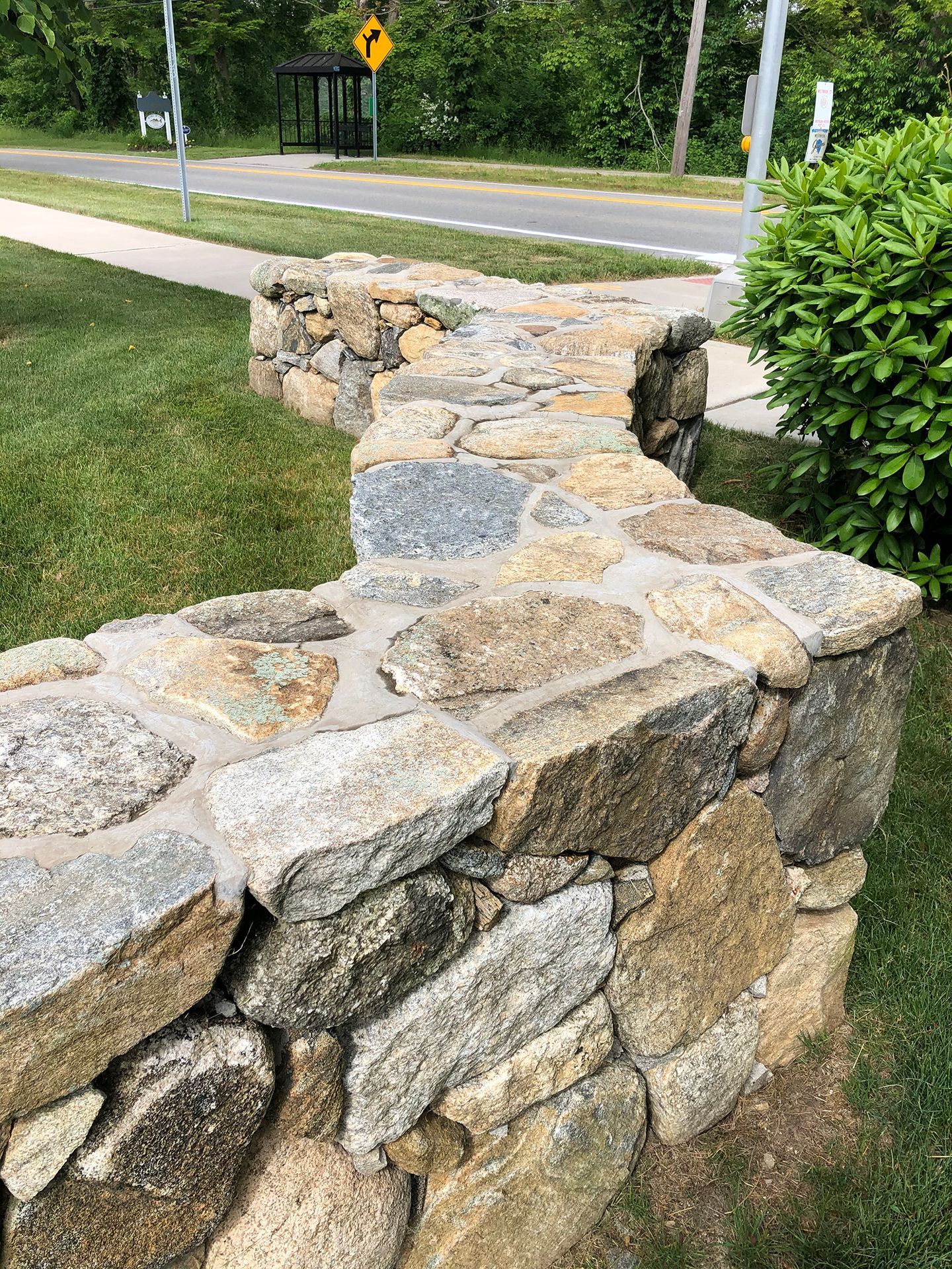 A stone wall is sitting in the grass next to a road.
