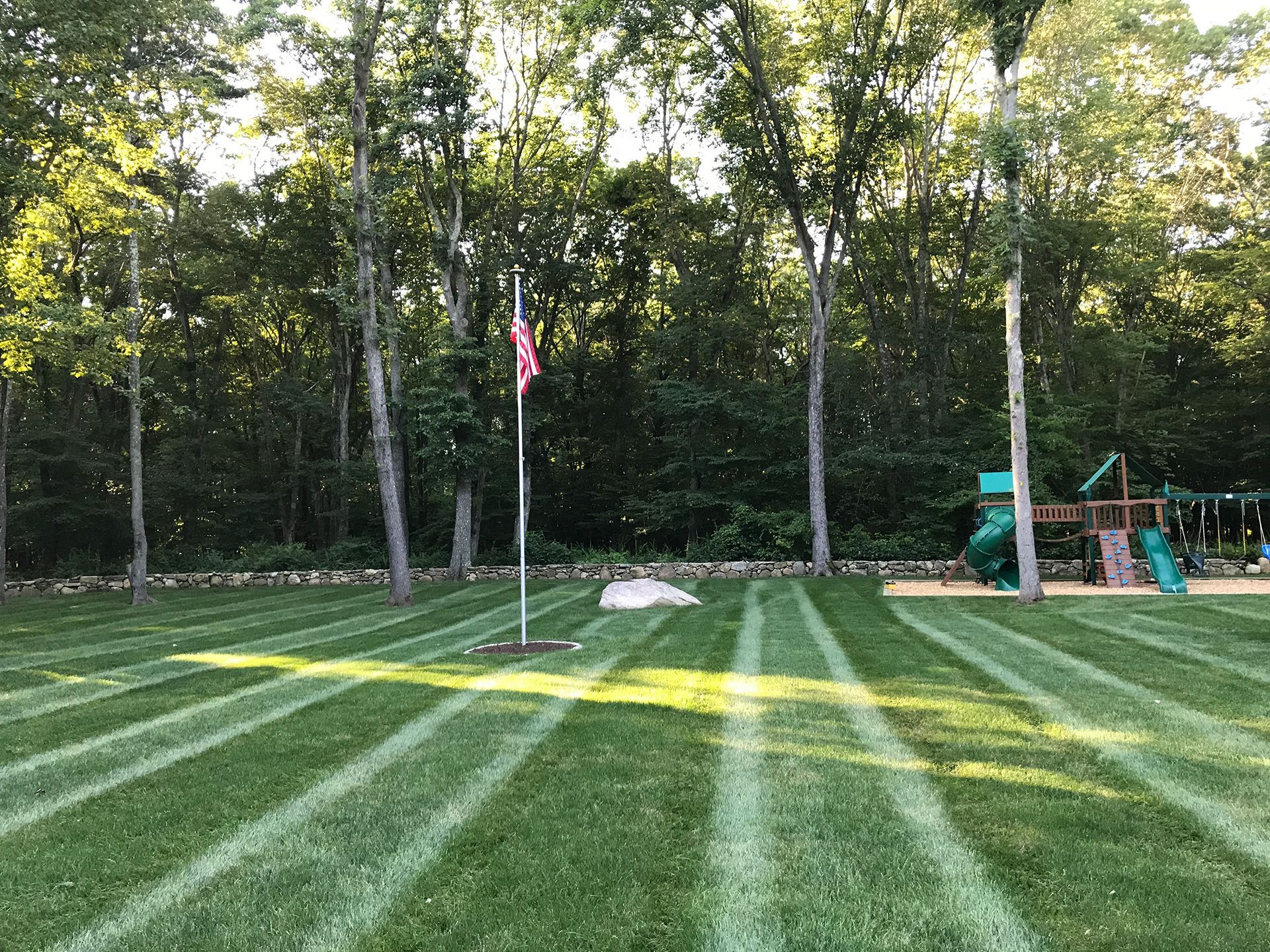 A lush green lawn with a playground in the background and a flag in the foreground.