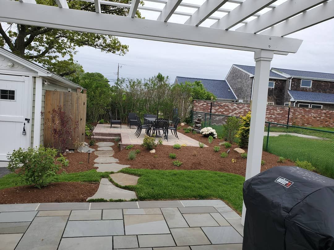 A backyard with a pergola, patio, table, and chairs.