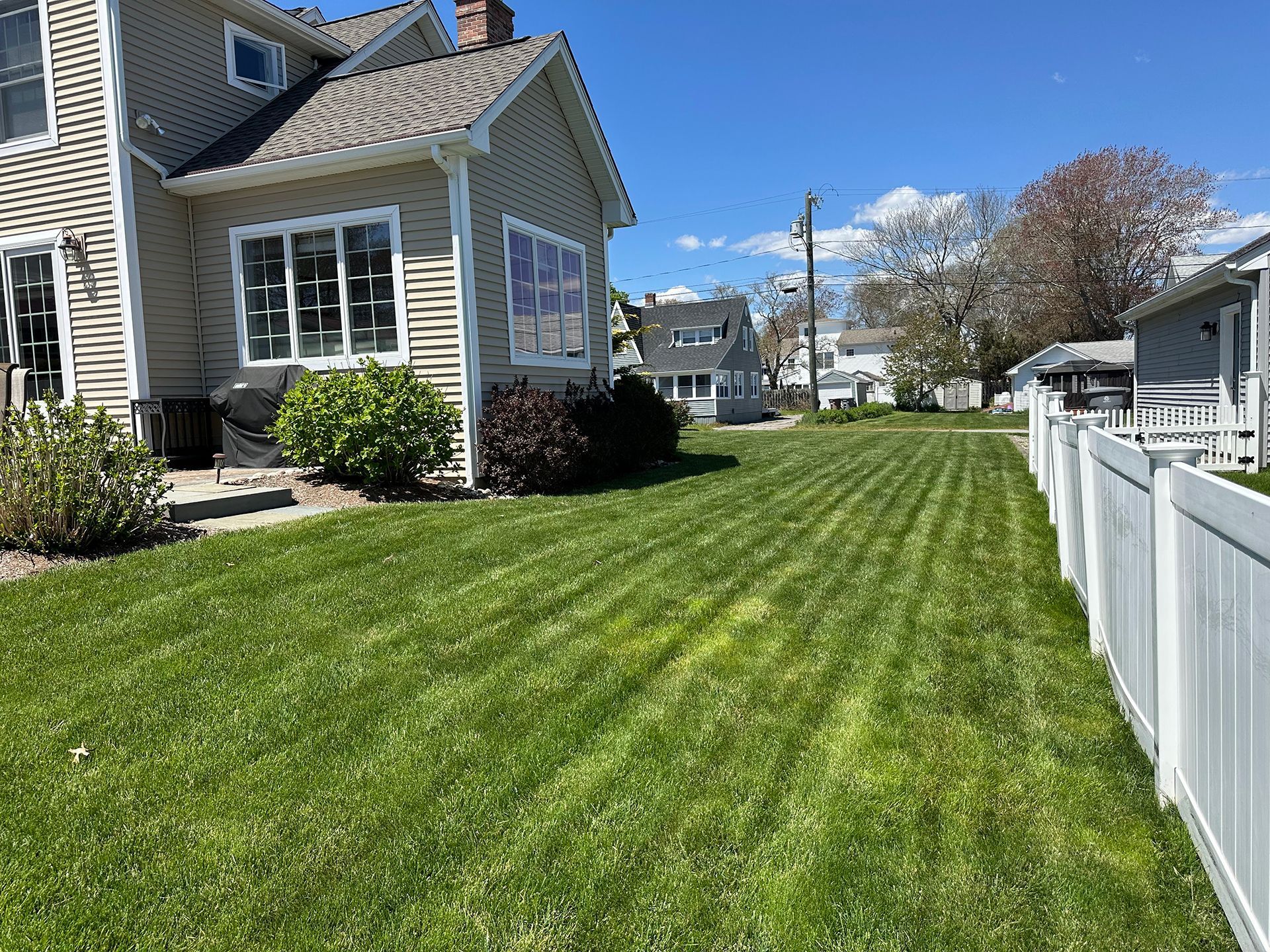 A house with a lush green lawn and a white fence in front of it.