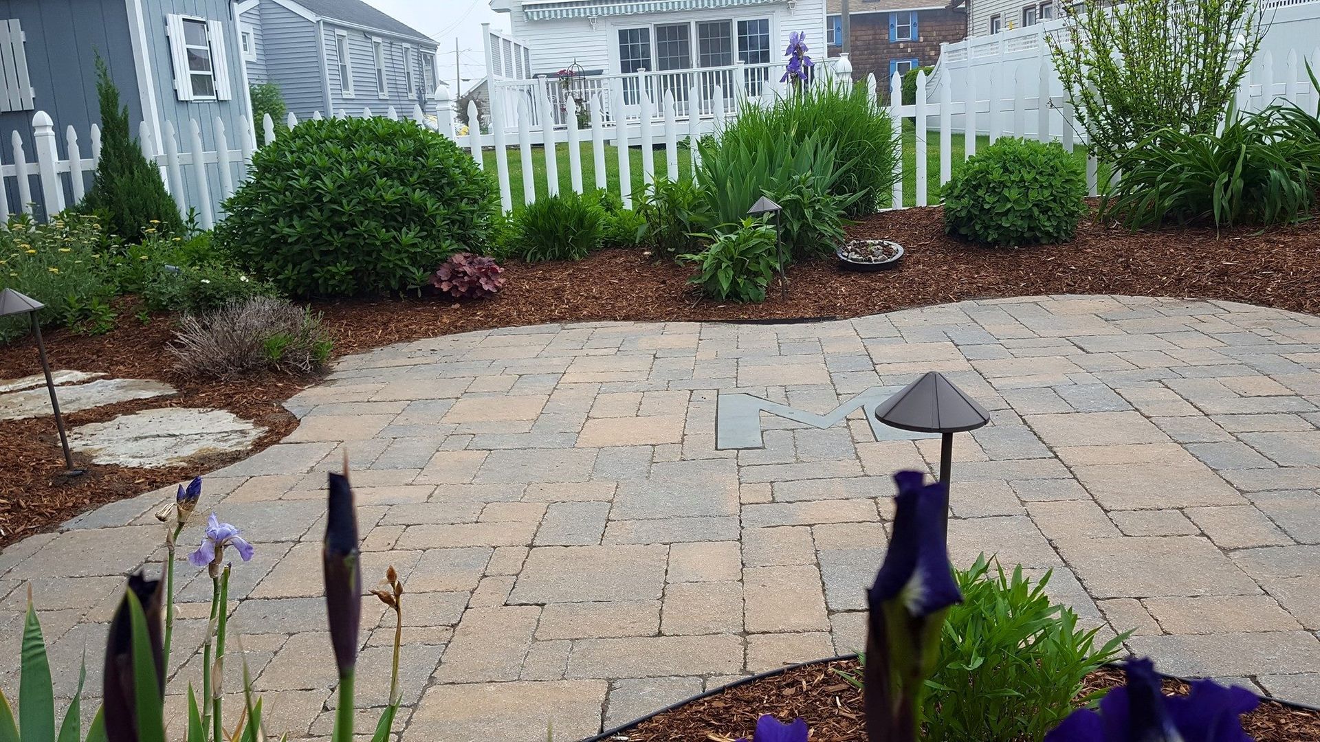 A patio with purple flowers and a white fence in the background