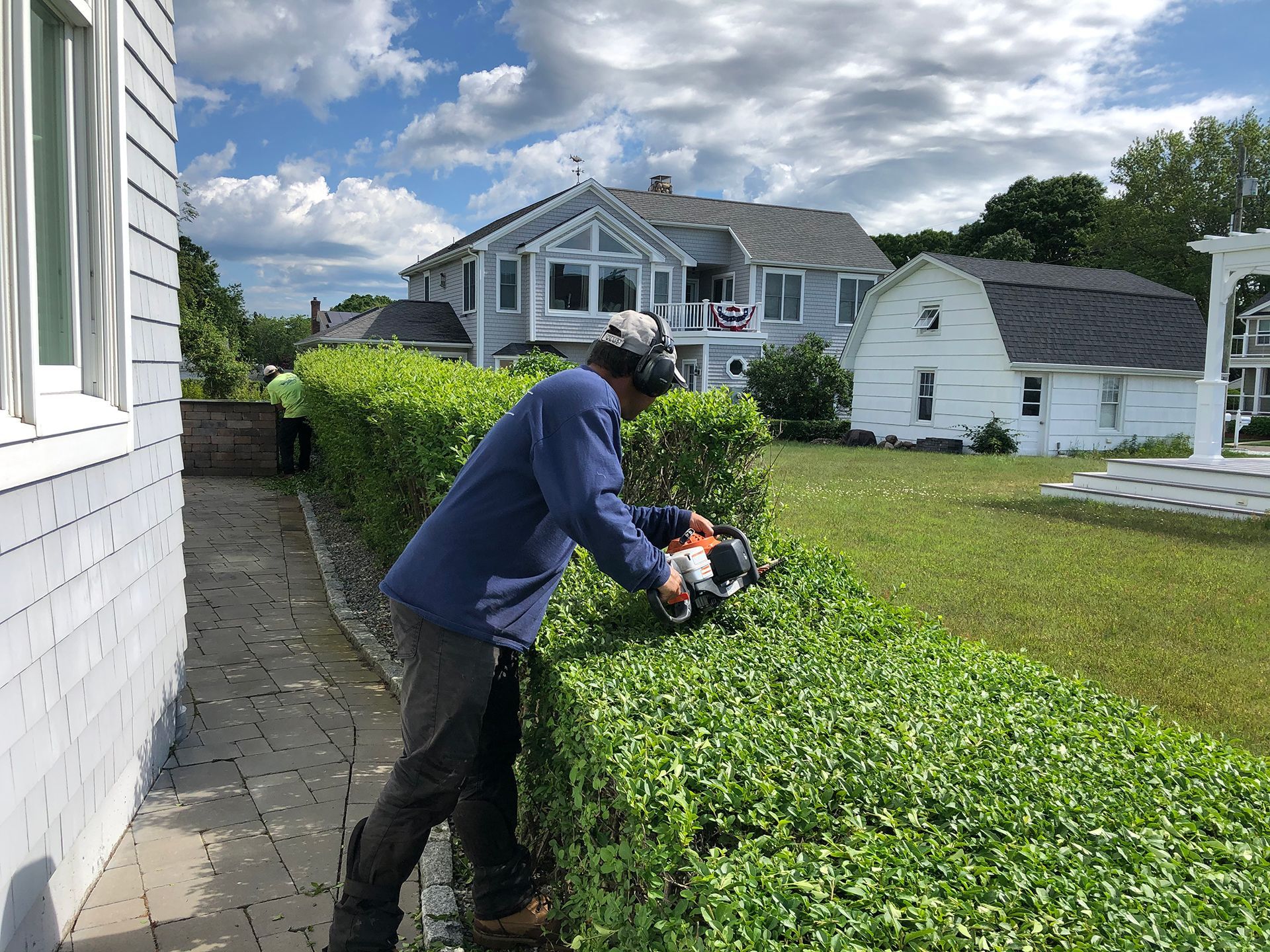 A man is cutting a hedge with a hedge trimmer in front of a house.