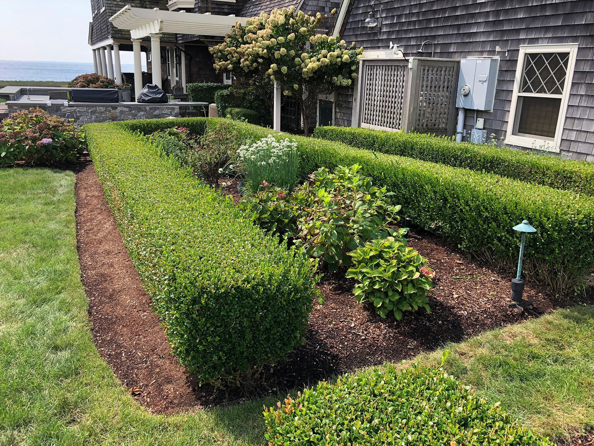 A lush green garden in front of a house with a view of the ocean.