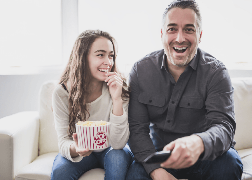 A man and a woman are sitting on a couch eating popcorn and watching tv