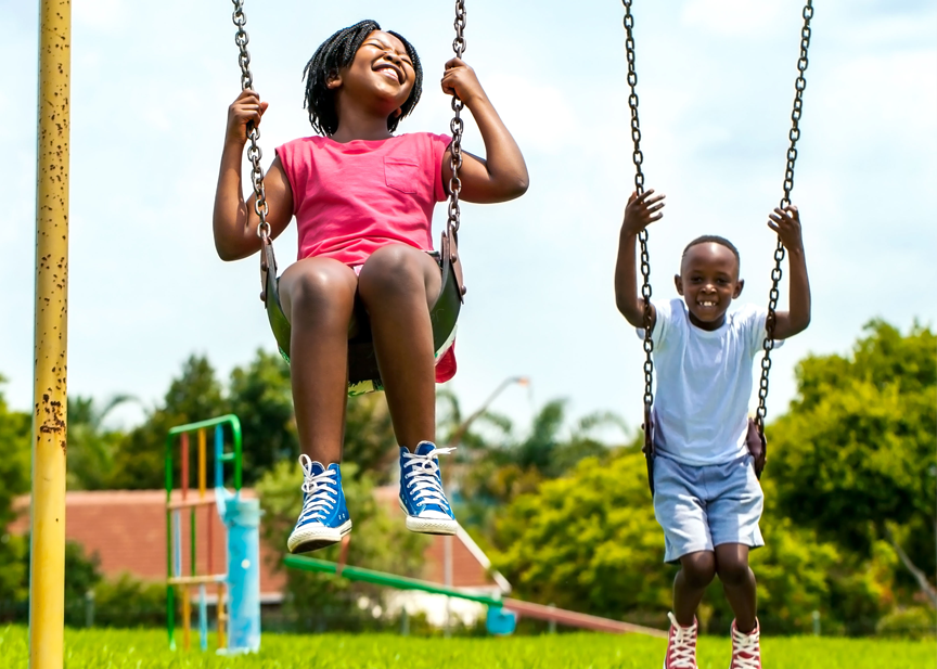 A boy and a girl are playing on swings in a park