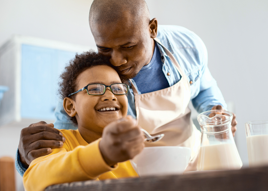 A man and a boy are eating cereal together in a kitchen