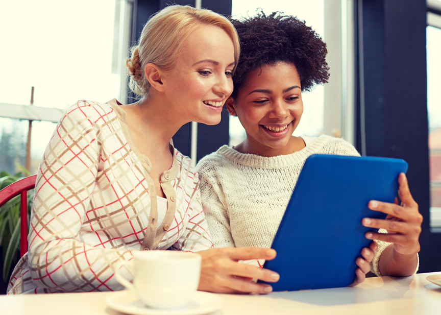 Two women are sitting at a table looking at a tablet