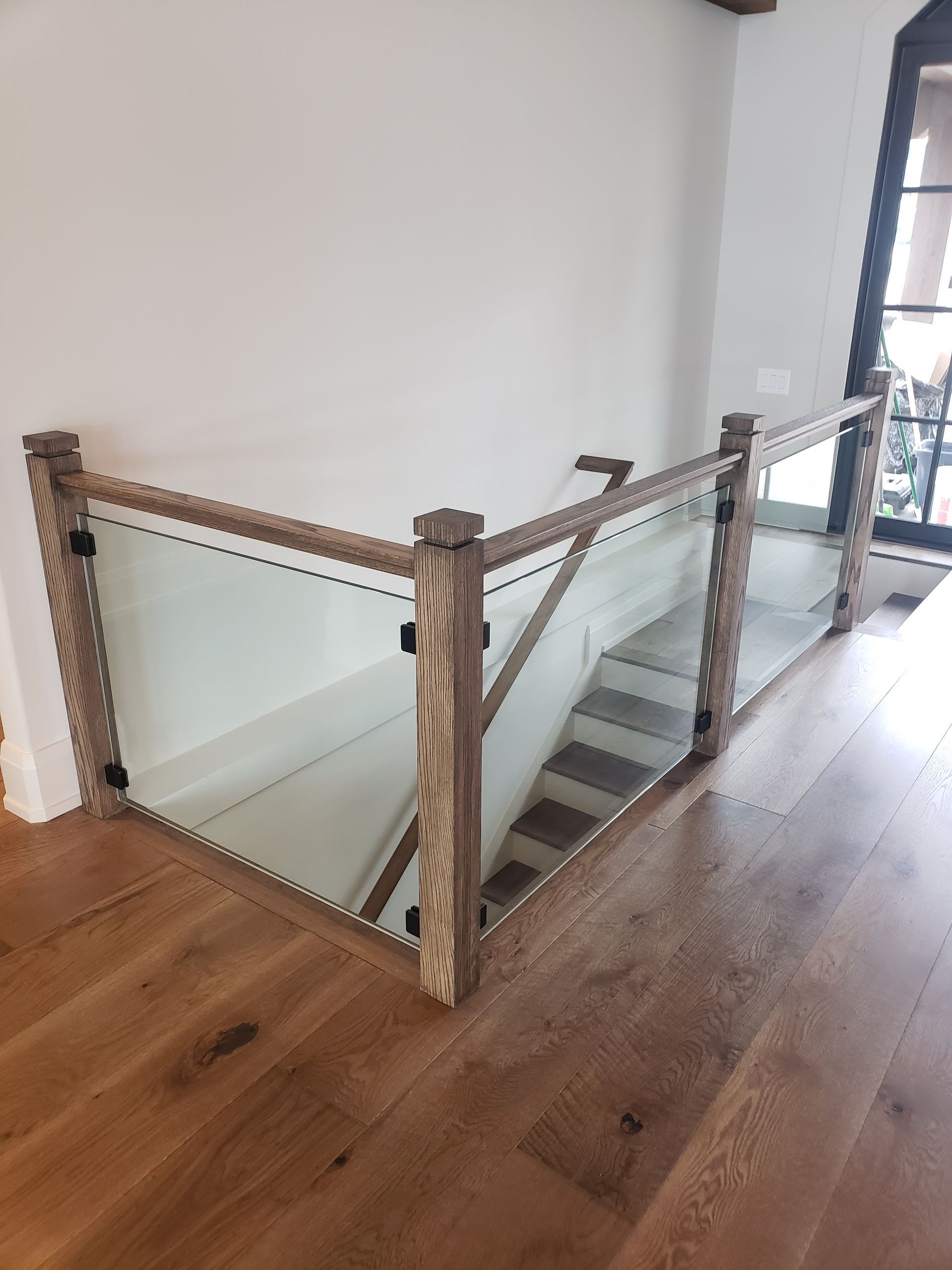 Wooden and glass railing surrounding a staircase with wood flooring.