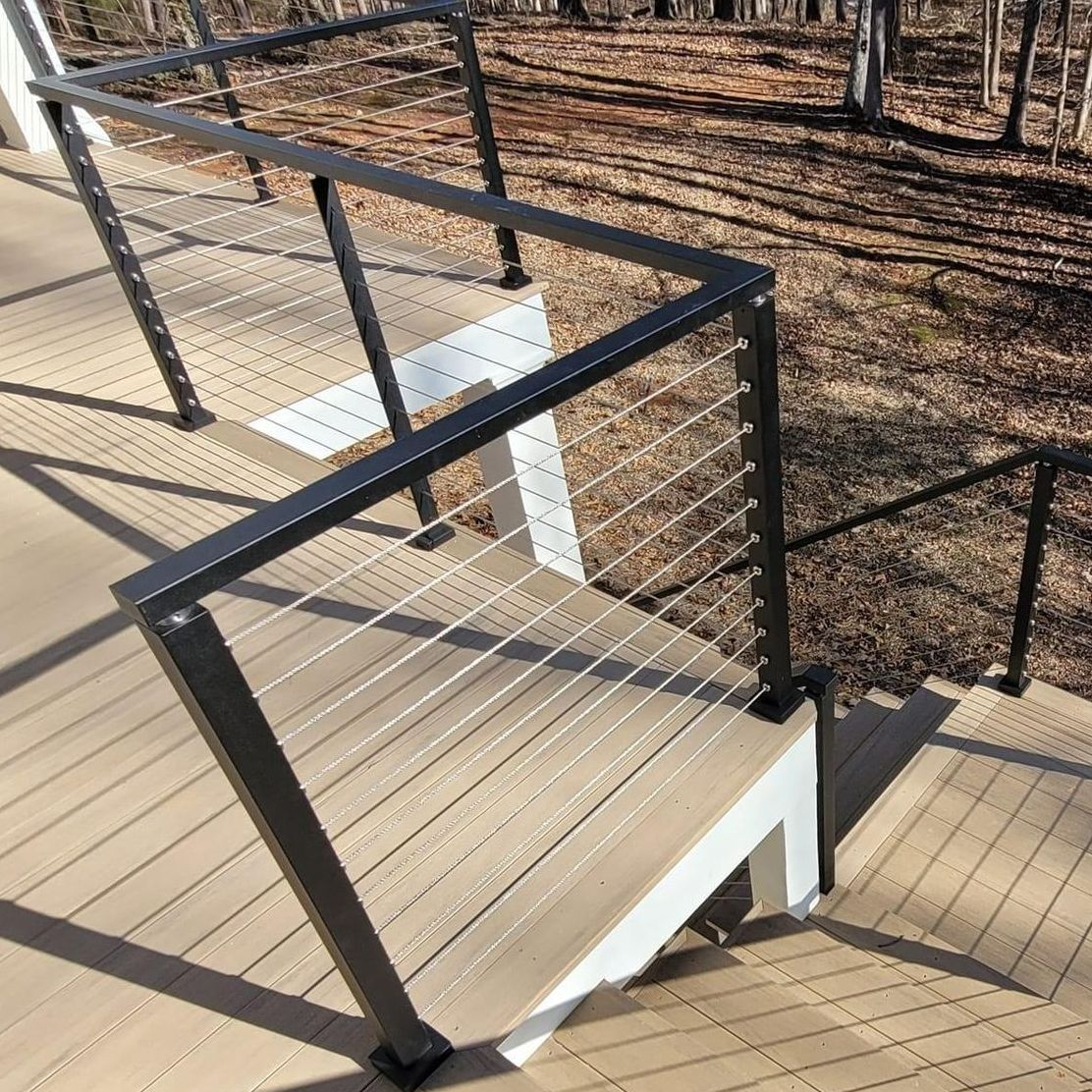 Deck stairs with black metal railings and wire infill; brown composite decking.