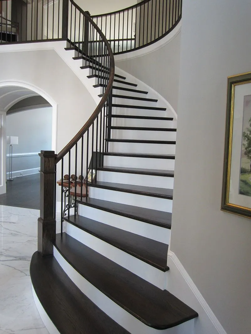 Dark wood curved staircase with white risers and black metal railing in a home.