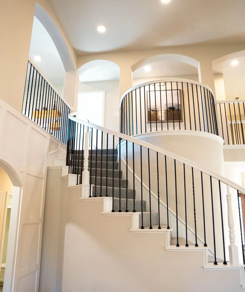 Staircase with black metal railings, leading to a second floor with arched openings. Beige and white tones.