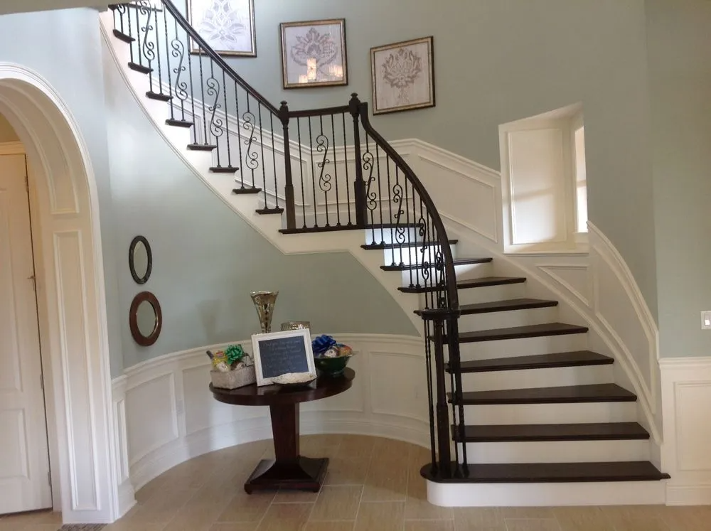 Elegant curved staircase with dark wood steps and wrought iron railing; light blue walls and decorative table.
