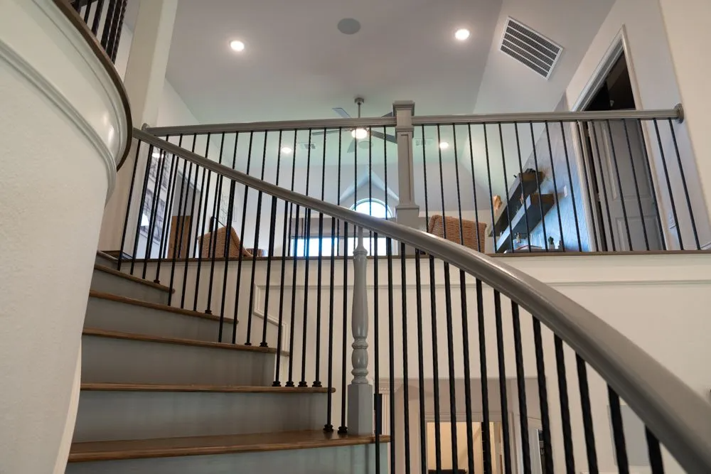 Staircase with gray steps and railing, black spindles, and a loft area with a railing and open windows.