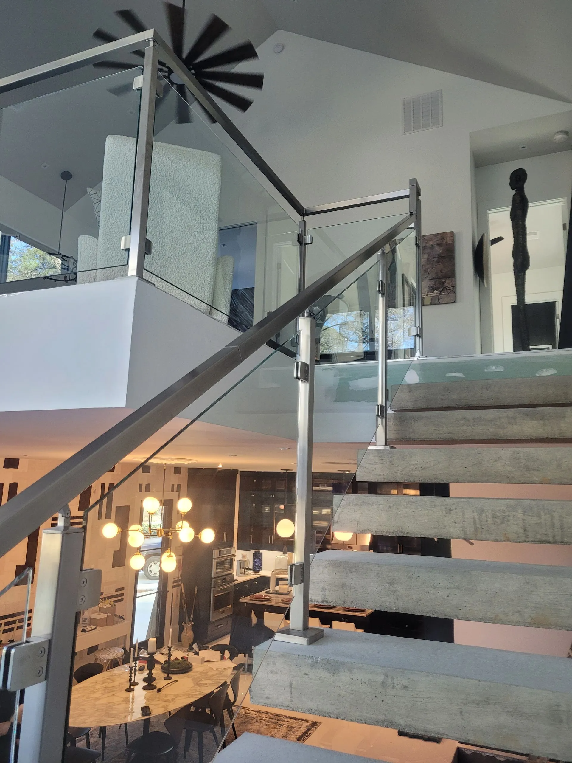 Staircase with glass railing leads to an upper level. Interior view with light fixtures and art.