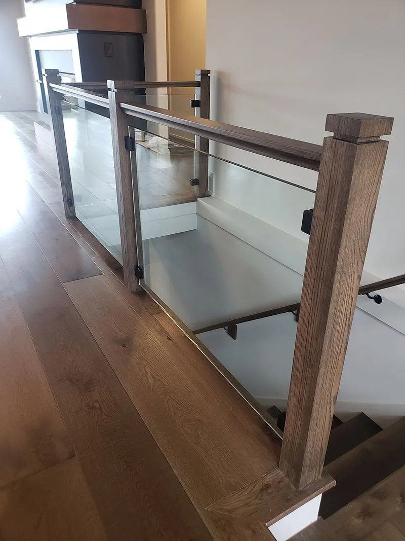 Wooden and glass railing beside a staircase, with hardwood flooring.