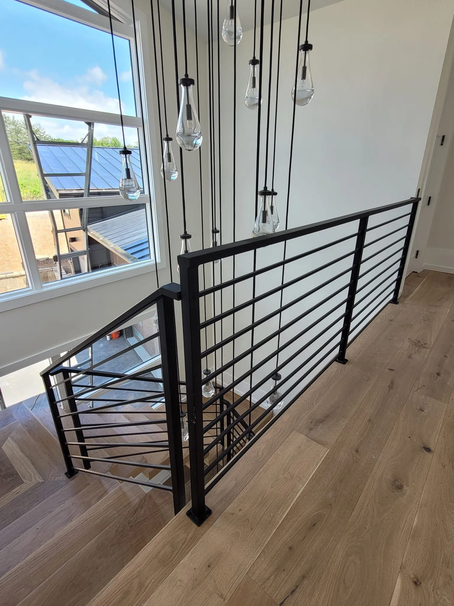 Interior view of a staircase with black metal railing, wooden steps, and large window.