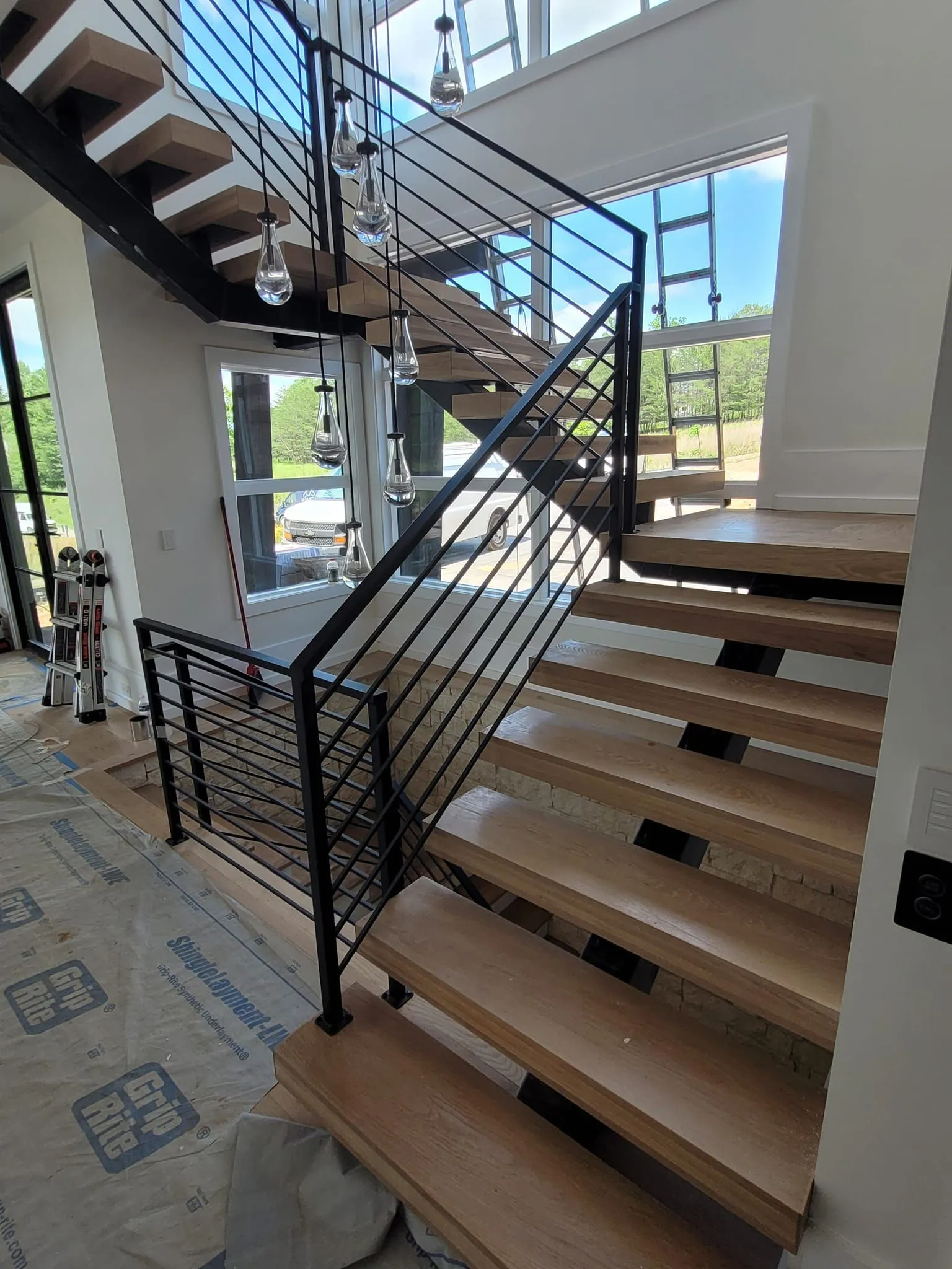 Modern wooden staircase with black metal railings and overhead lighting.
