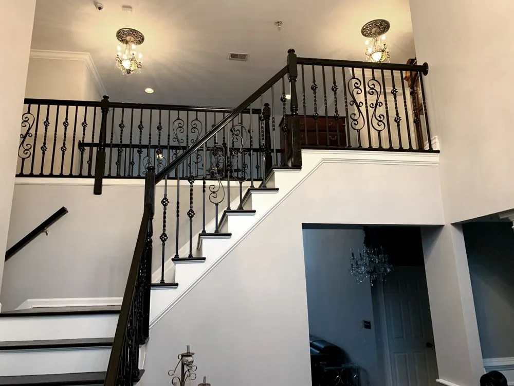 Staircase with black wrought iron railings, white steps, and a landing with similar railings.