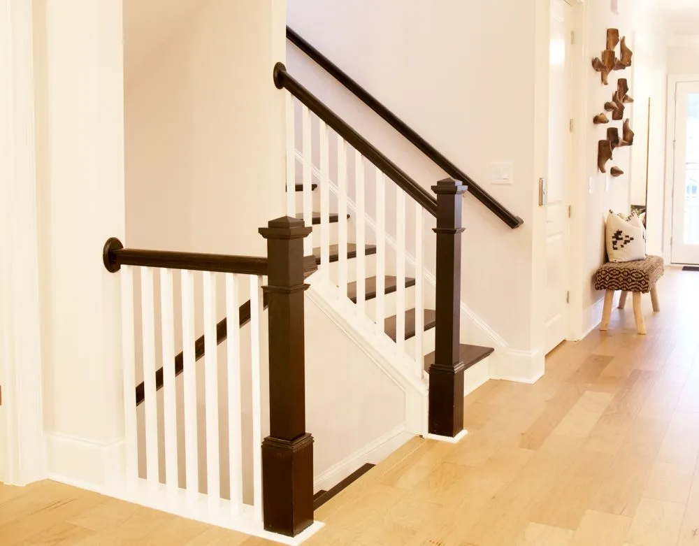 Staircase with white balusters, dark handrails and newel posts in a well-lit interior with hardwood floors.