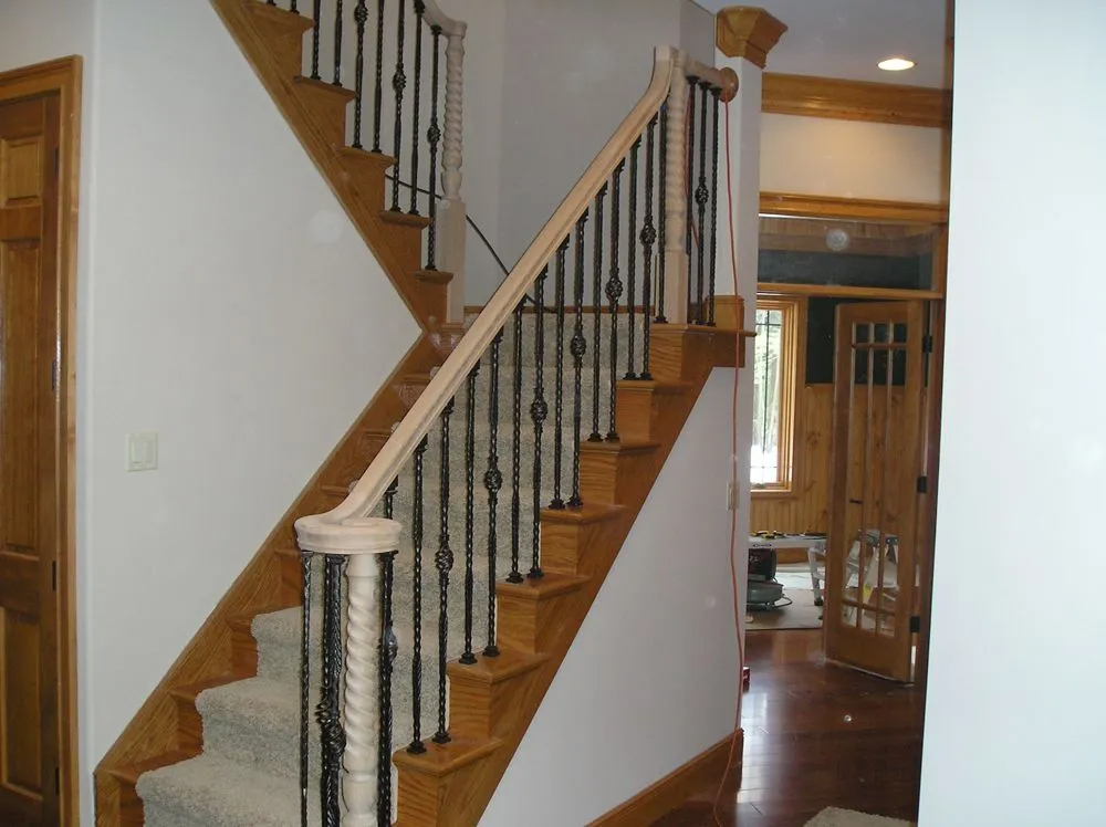 Staircase with wooden steps and railing, black iron spindles, leading to a doorway.