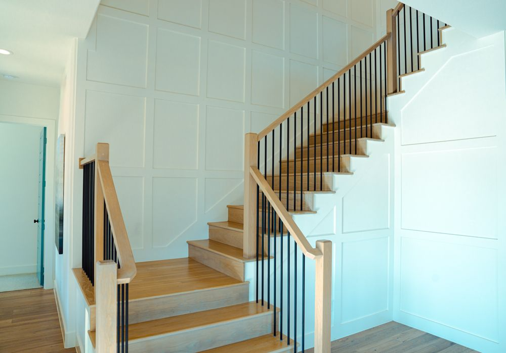 Staircase with light wood steps, black iron spindles, and white paneled walls.