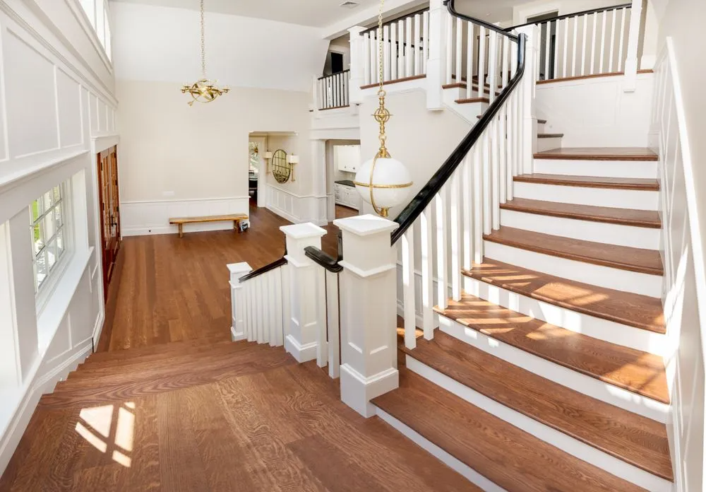 Grand foyer with wooden staircase, white walls, and decorative light fixtures.