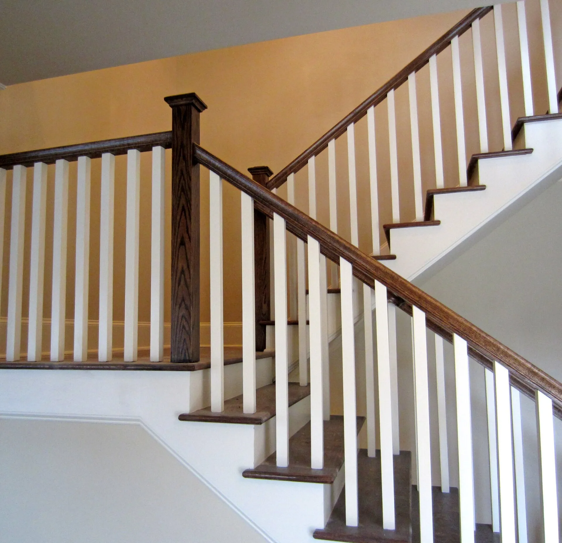 Staircase with white balusters, brown wooden handrails, and beige walls.
