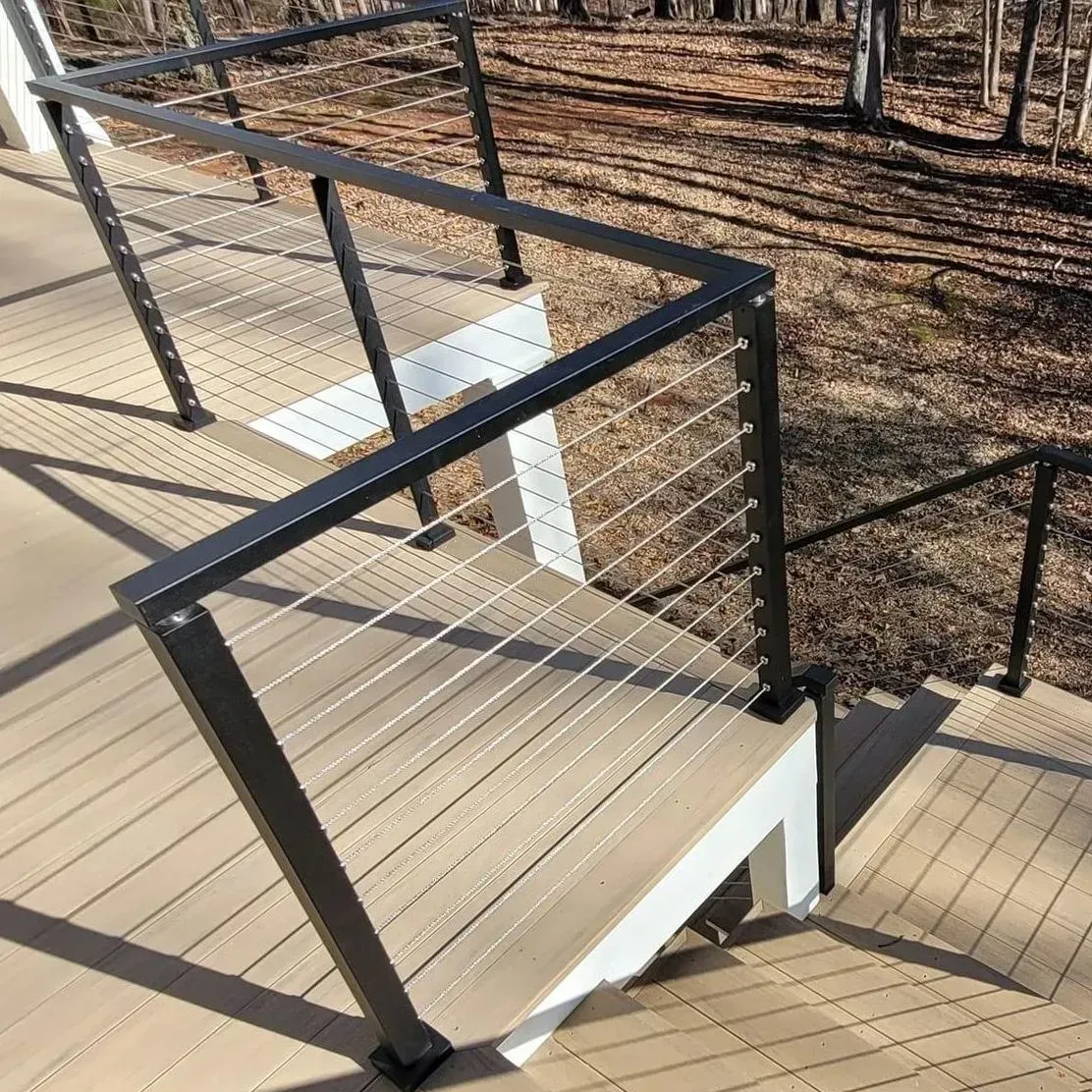 Outdoor staircase with composite decking and black metal cable railings.