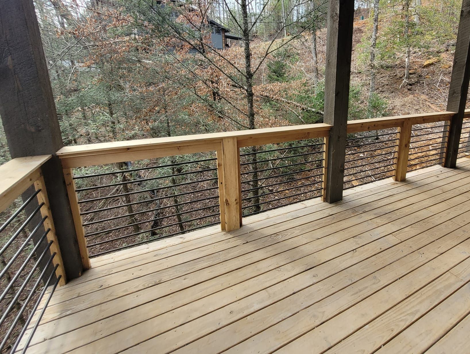 Wooden deck with cable railing overlooking a wooded area.