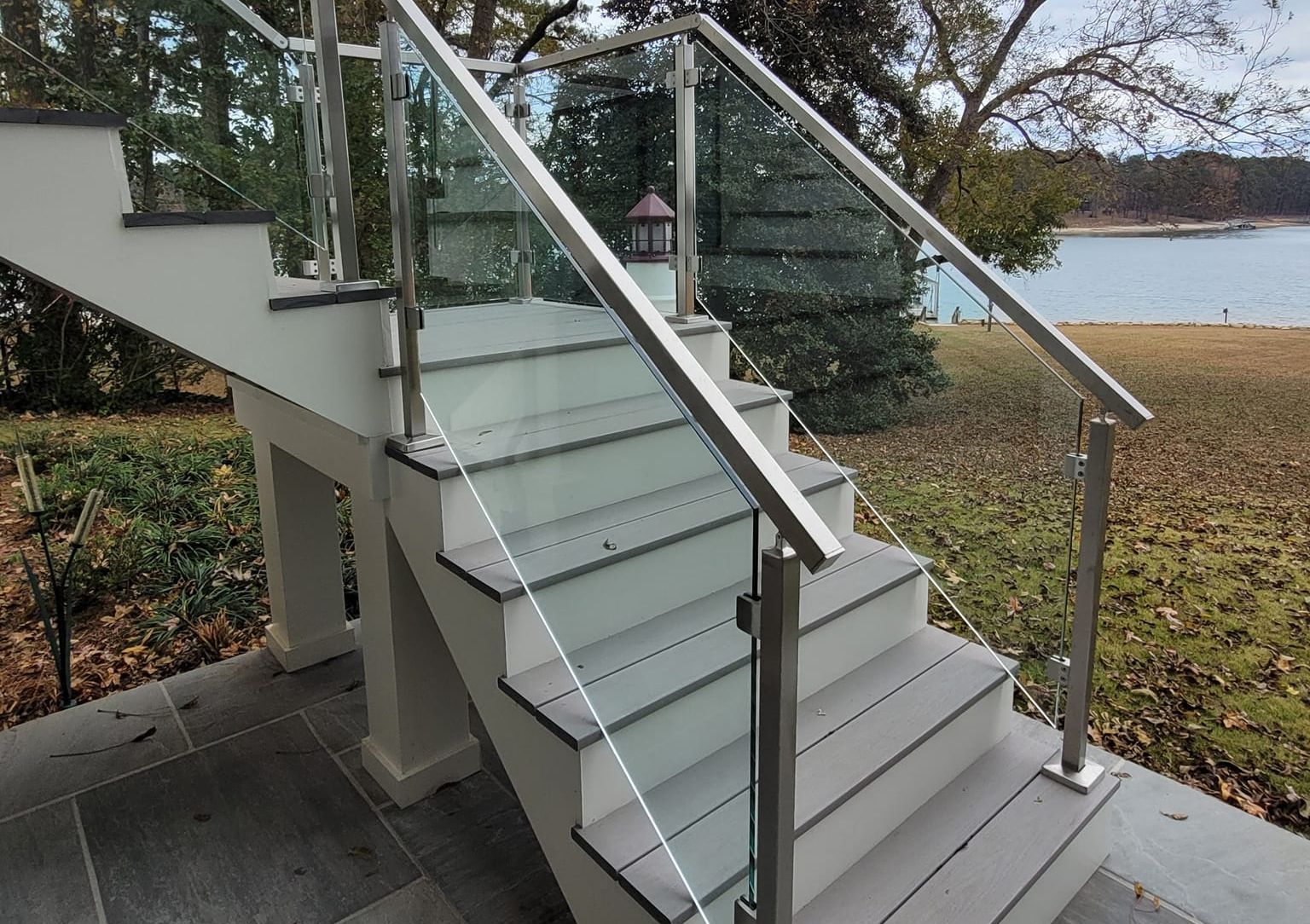 Outdoor staircase with glass and metal railing overlooking a lake.