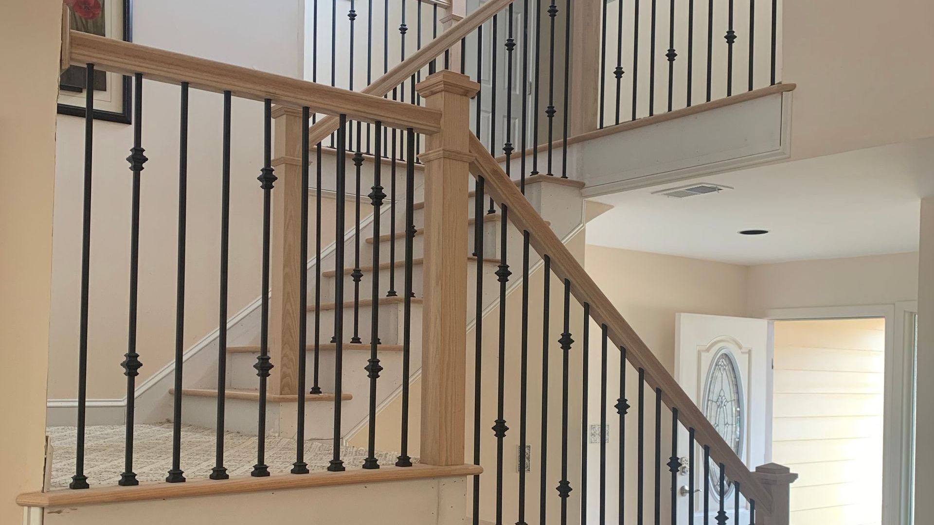 Staircase with wooden handrails and black iron balusters in a home setting.