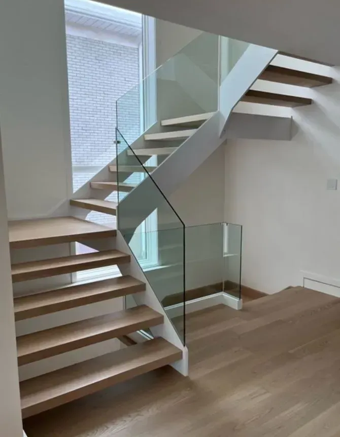 Modern staircase with wood steps, glass railing, white support structure, and natural light.