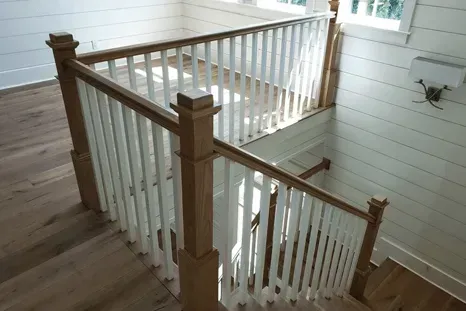 Staircase with white balusters and wooden handrails, leading down into a white-walled room with wooden floors.