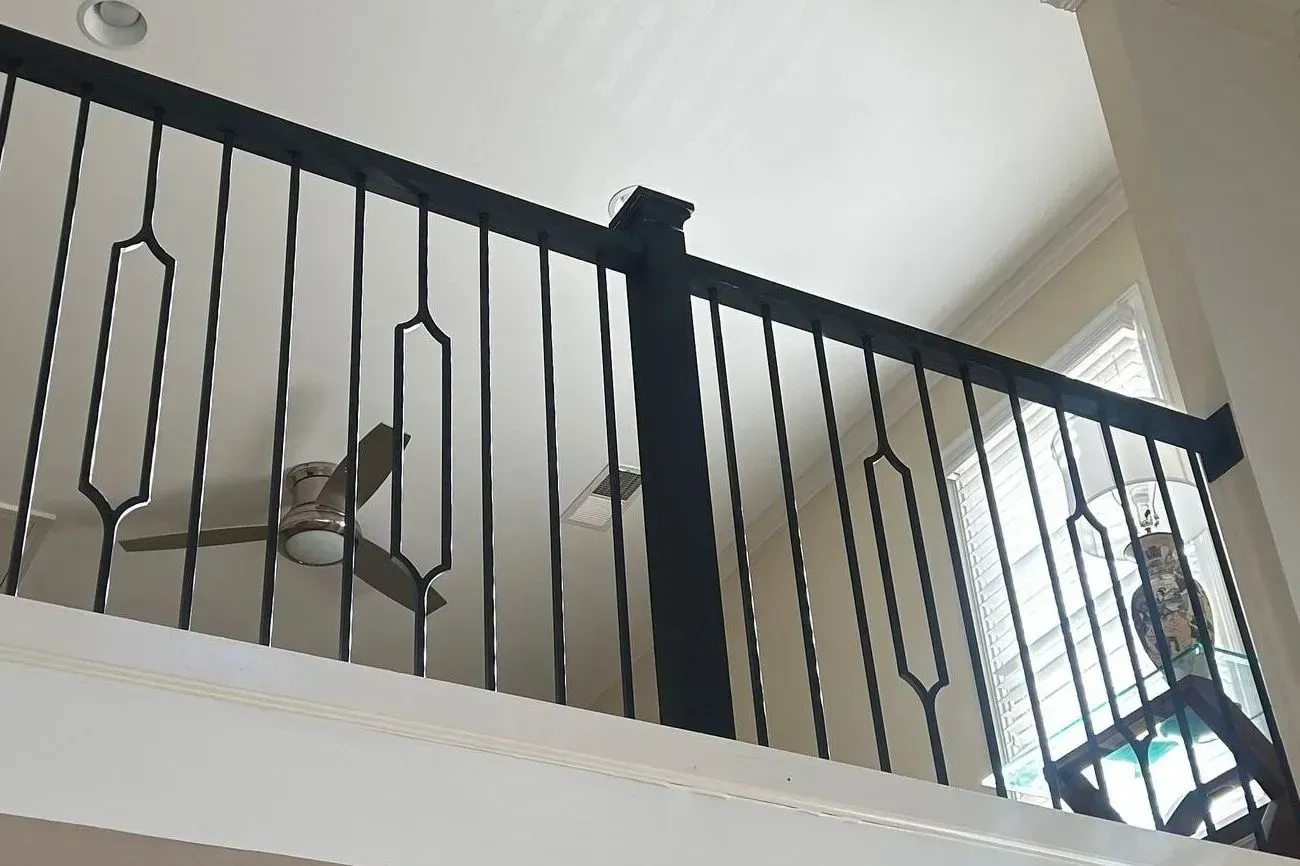Black railing with decorative cutouts, inside a home. A ceiling fan is visible.