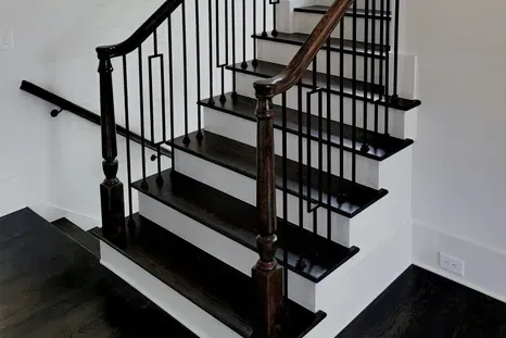 Dark wooden staircase with black metal railings and white risers.