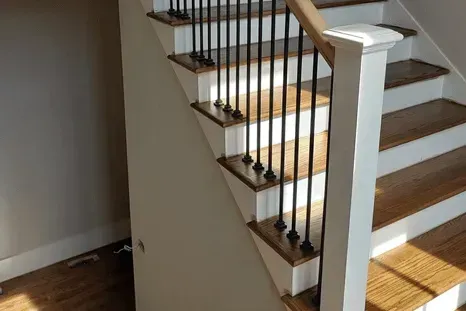 Staircase with wooden steps, white risers, black metal balusters, and a wooden handrail.