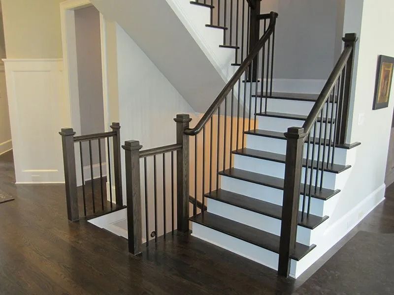Staircase with wooden handrails and black iron balusters in a home setting.