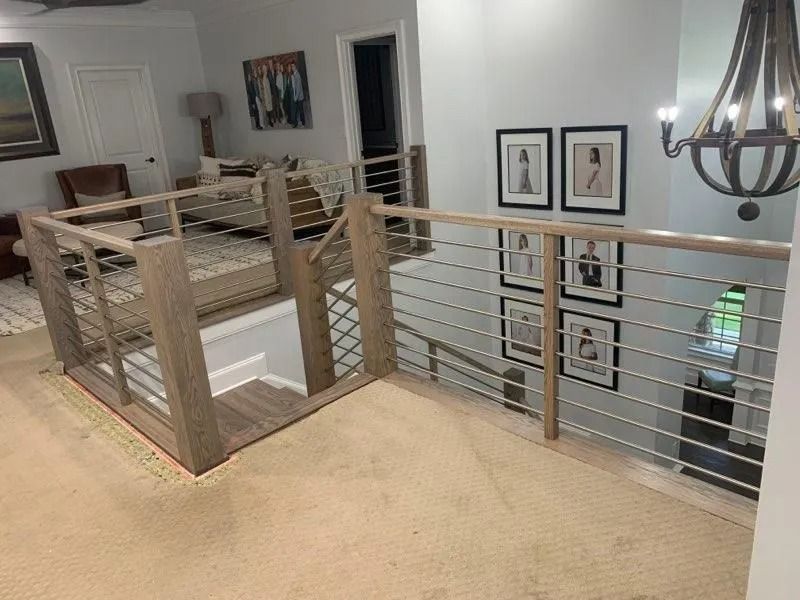 Interior view of a house with a stairway and cable railing. Light-colored walls, neutral carpet, and artwork are visible.