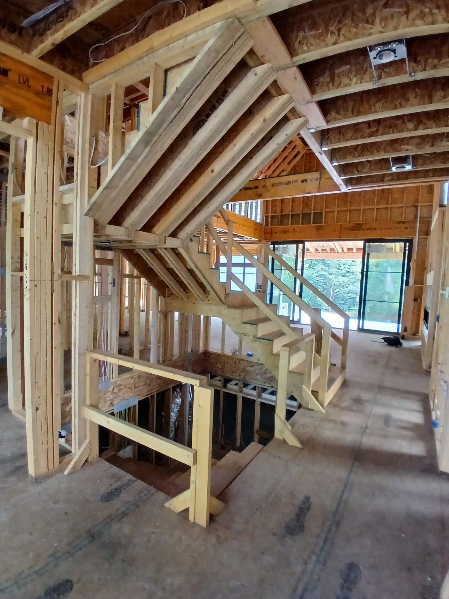 Wooden staircase under construction inside a building; unfinished walls, beams, and steps visible.