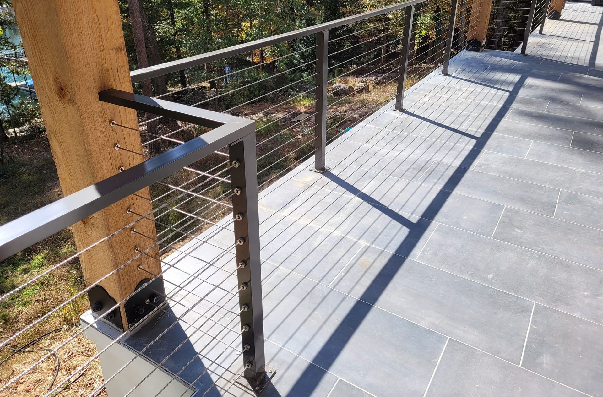 Deck with gray flooring, metal railing, and horizontal steel cables. Brown wooden supports.