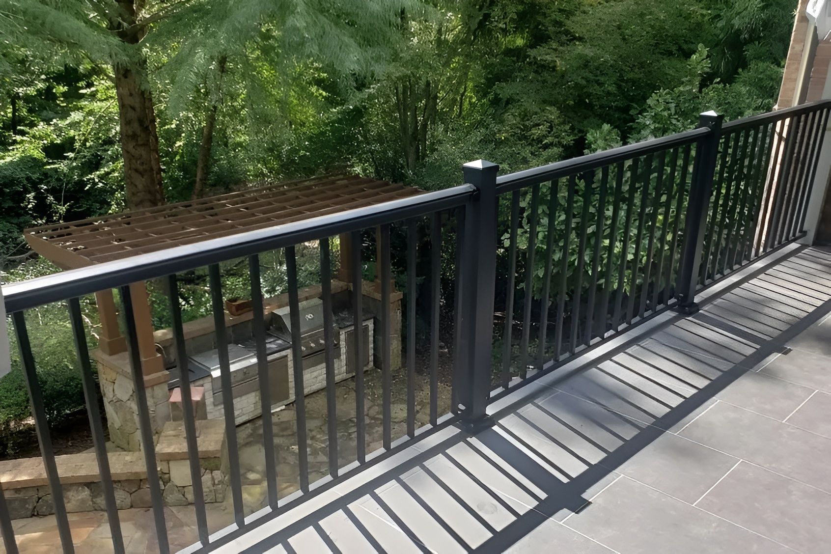 Black metal deck railing with vertical bars, overlooking a natural green landscape.