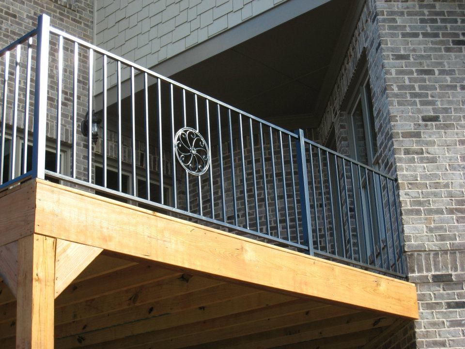 A wooden deck with a metal railing, attached to a brick building.