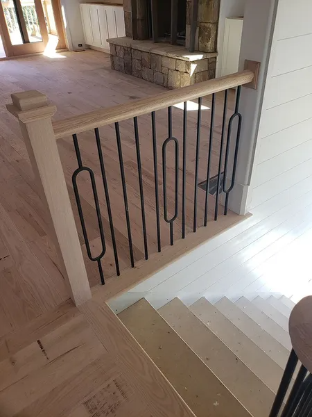 Staircase with wooden railing and black metal spindles with decorative oval shapes.