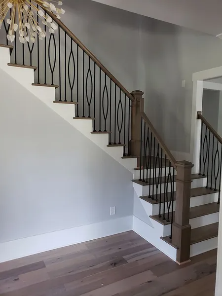 Staircase with light wood steps, dark spindles, and a wooden handrail, leading up against a light grey wall.