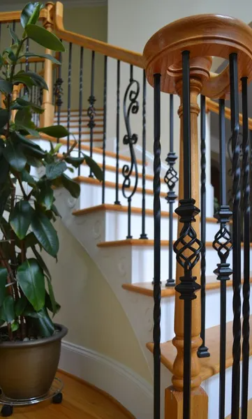 Staircase with wooden railing, black iron balusters, and a potted plant.
