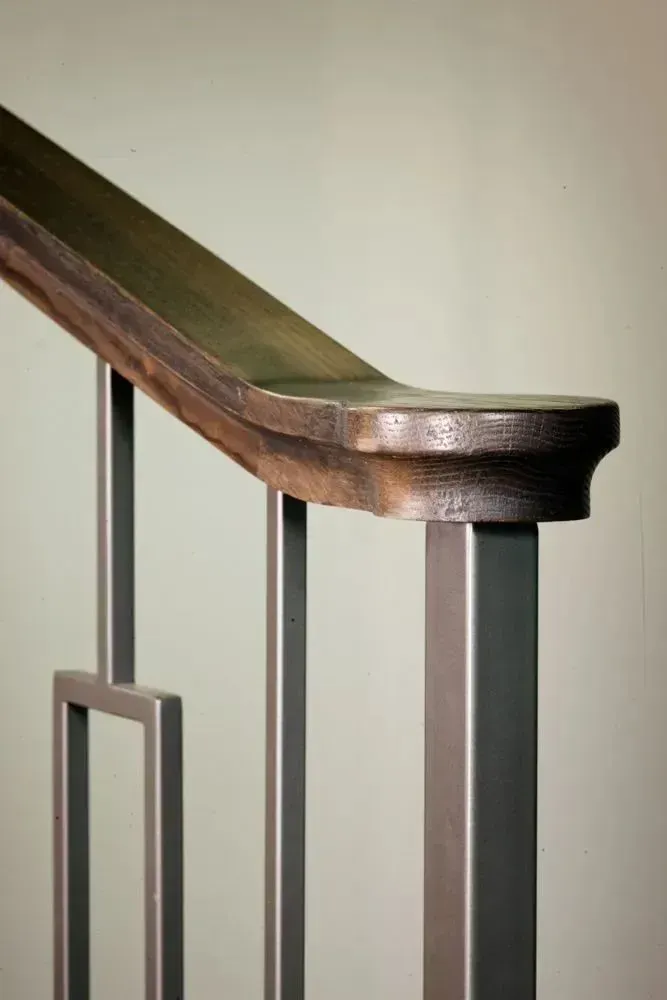 Close-up of a metal railing with a dark wood handrail, against a light green wall.