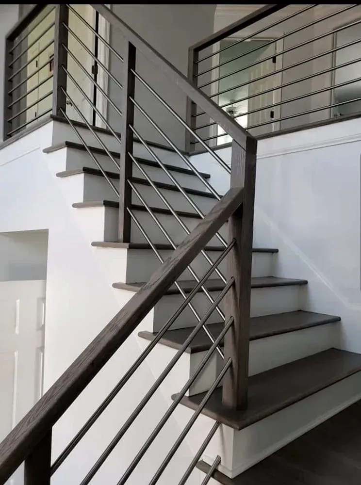 Staircase with wooden handrails and metal bars, leading to an upper level. White walls.
