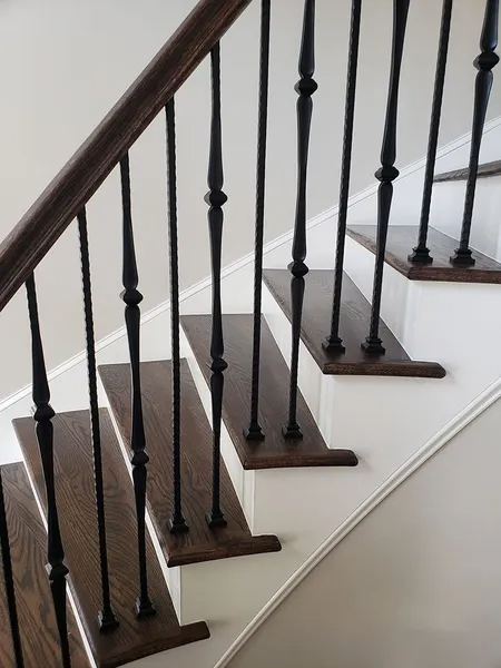 Staircase with dark wood treads and handrail, black spindles, white risers, and a neutral wall.